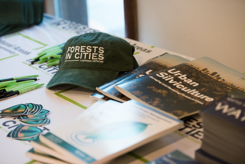 A baseball hat with "Forests in Cities" logo, pens, and booklets on a table.