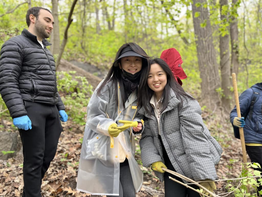 Two volunteers smiling wearing safety gloves, one holds a branch