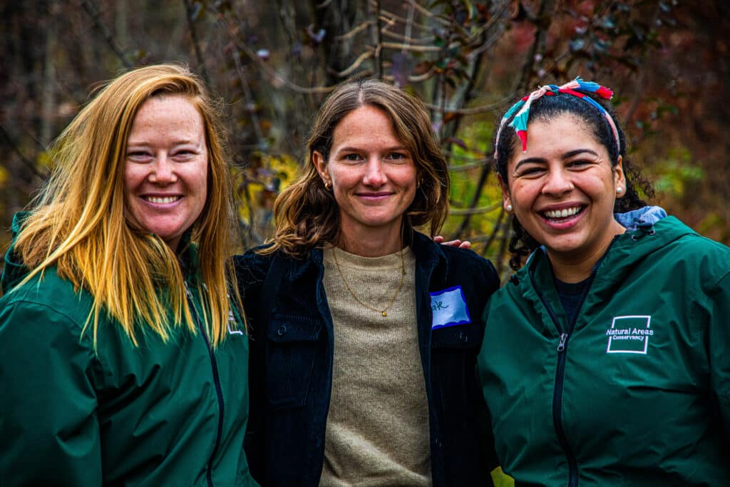 Three staff members smiling with foliage in the background.
