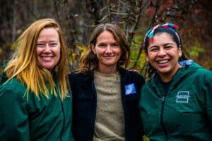 Three staff members smiling with foliage in the background.