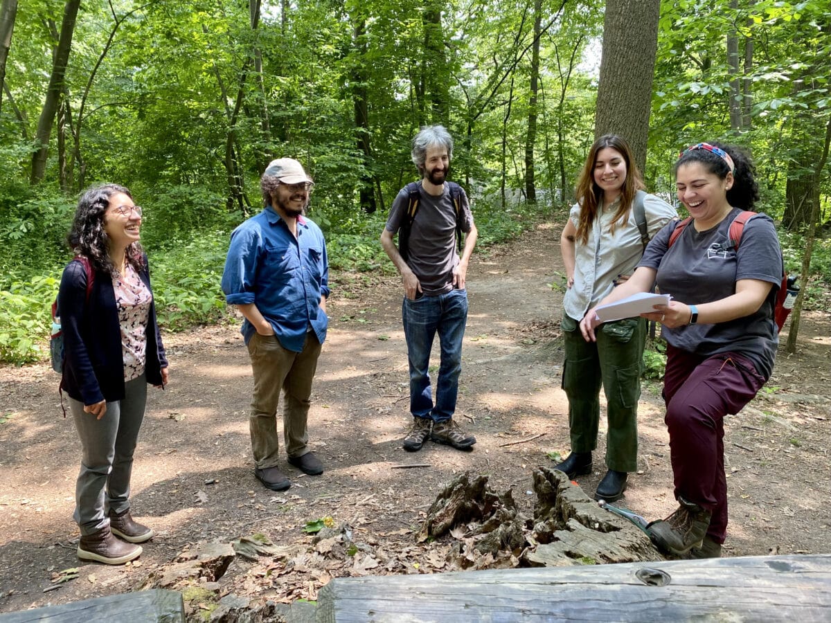 A group of 5 staff members stand in a semi-circle smiling on a forest trail