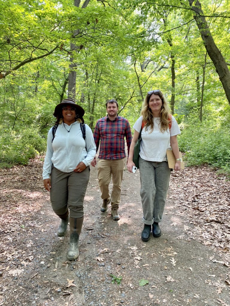 Staff members Naiyiri, Sam, and Clara walk on gravel path in forest