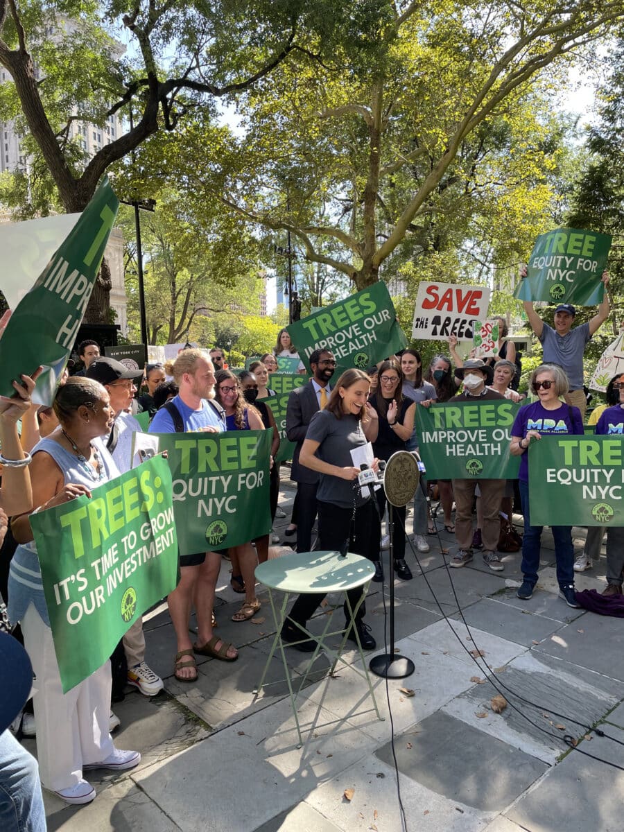 Sarah Charlop-Powers walks towards microphone in front of City Hall, surrounded by ralliers holding “Tree equity” signs