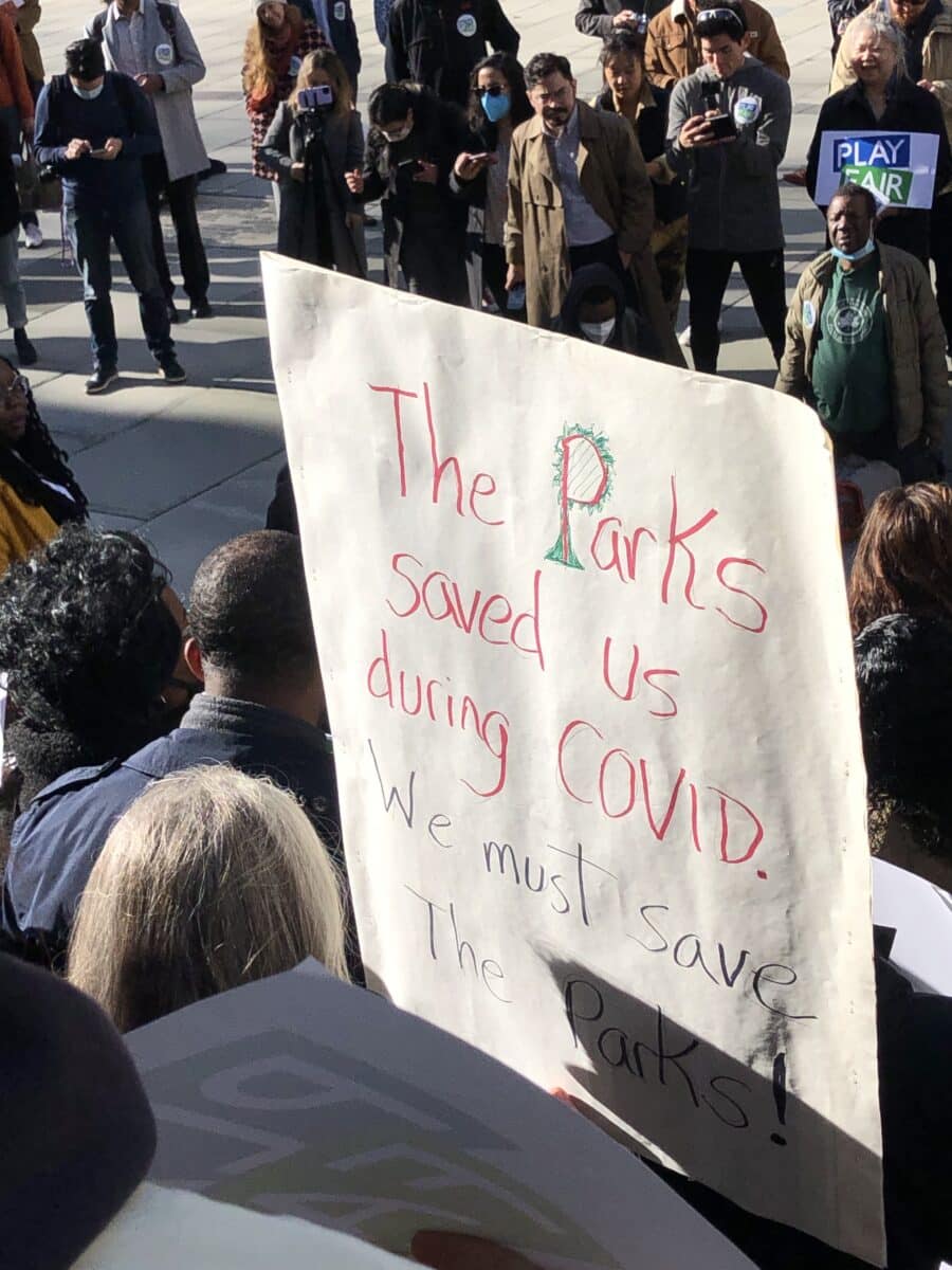A sign is held up at a rally that reads “The Parks saved us during covid, we must save the parks”