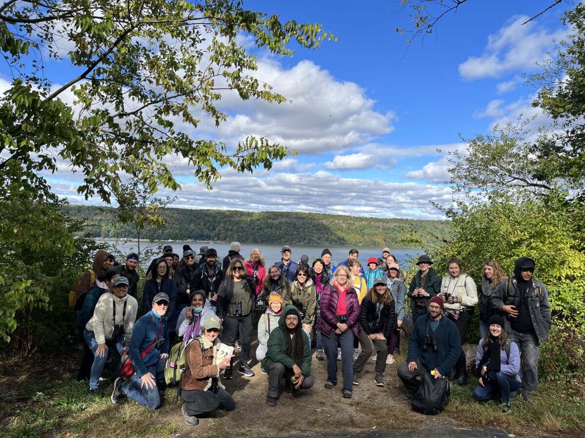 A large group of park sightseers led by NAC pose in Inwood Hill Park with Hudson River in background