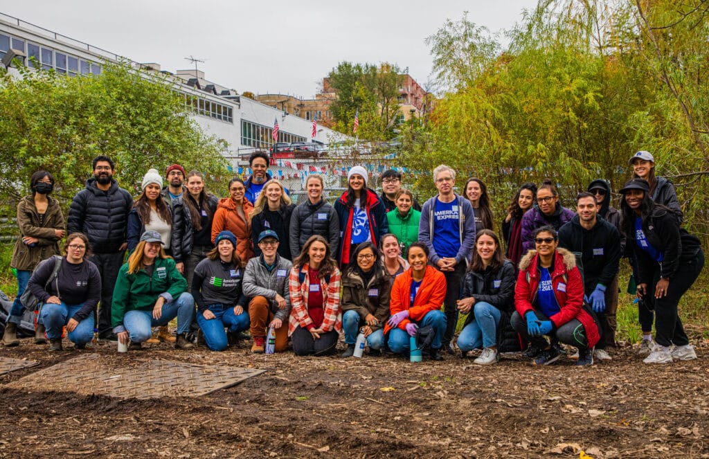 A large group of volunteers and NAC staff stand in rows, smiling in a park with fall foliage