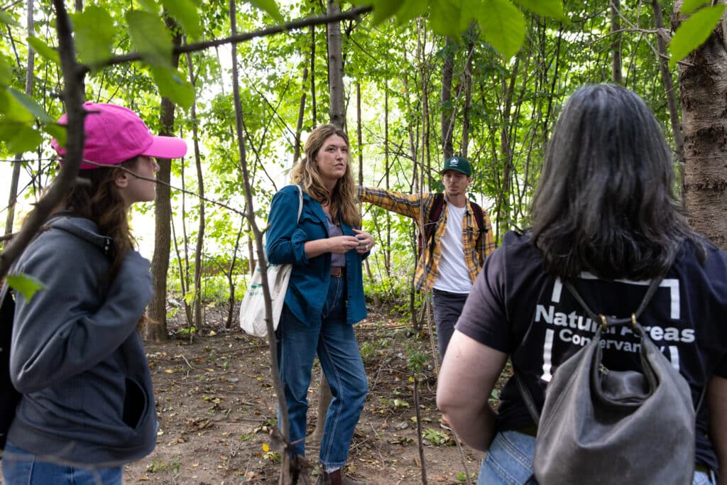Deputy Director of Conservation Science, Clara Pregitzer addresses a larger group of colleagues in a forest