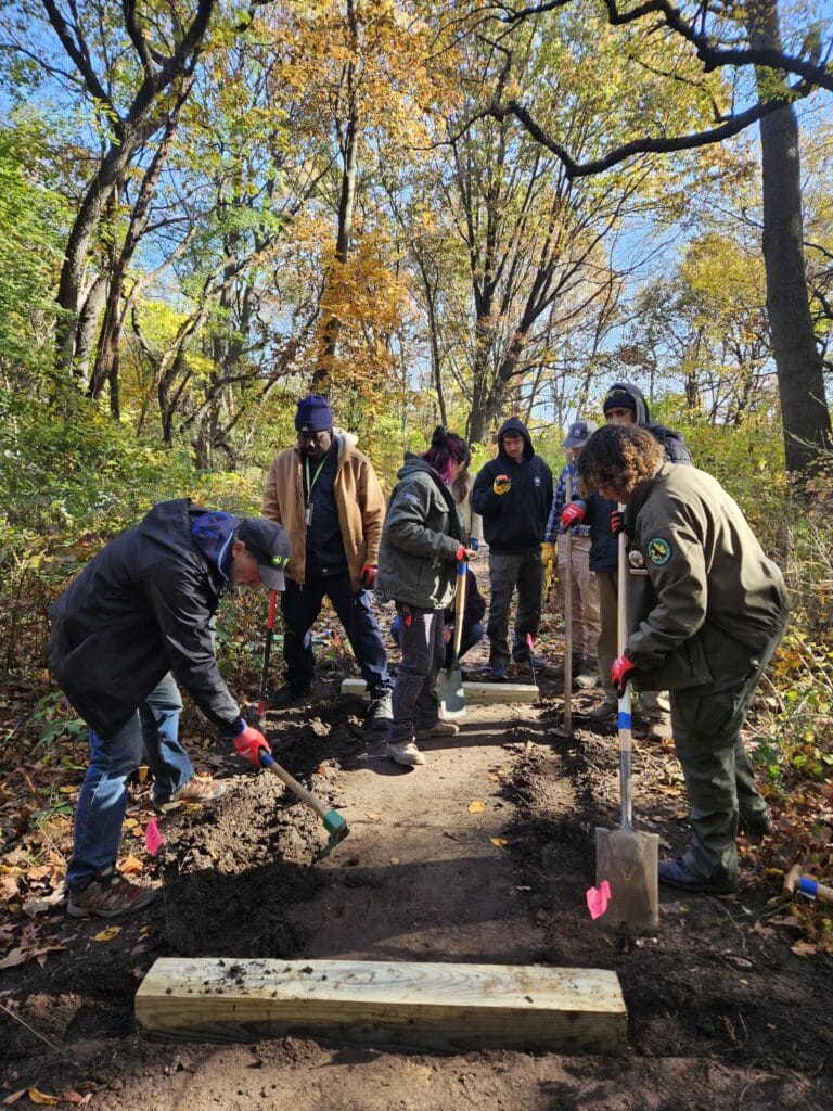 A trails crew clear a path by raking dirt on a fall day