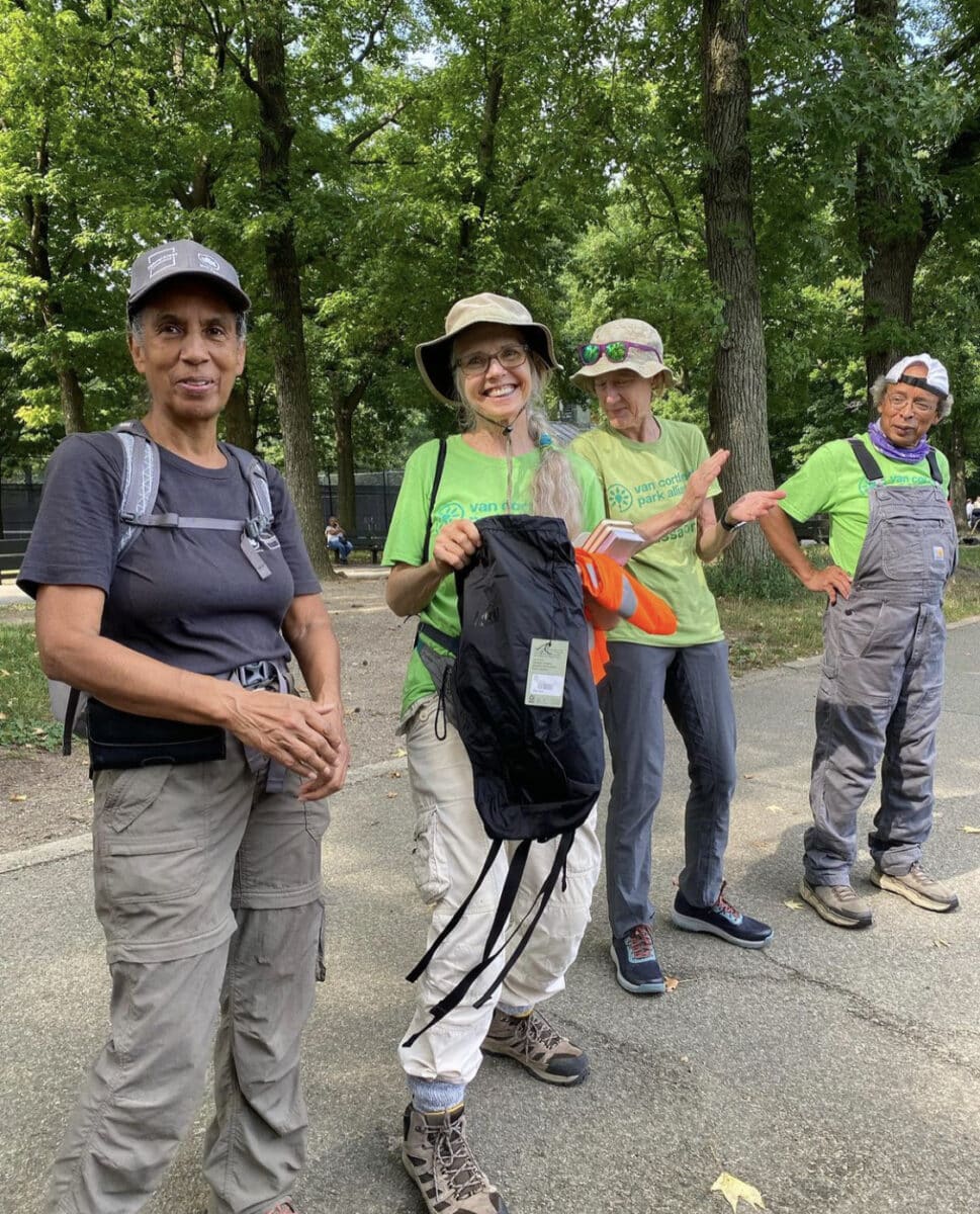 A group of four trail maintainers wear green t-shirts smiling in a public park