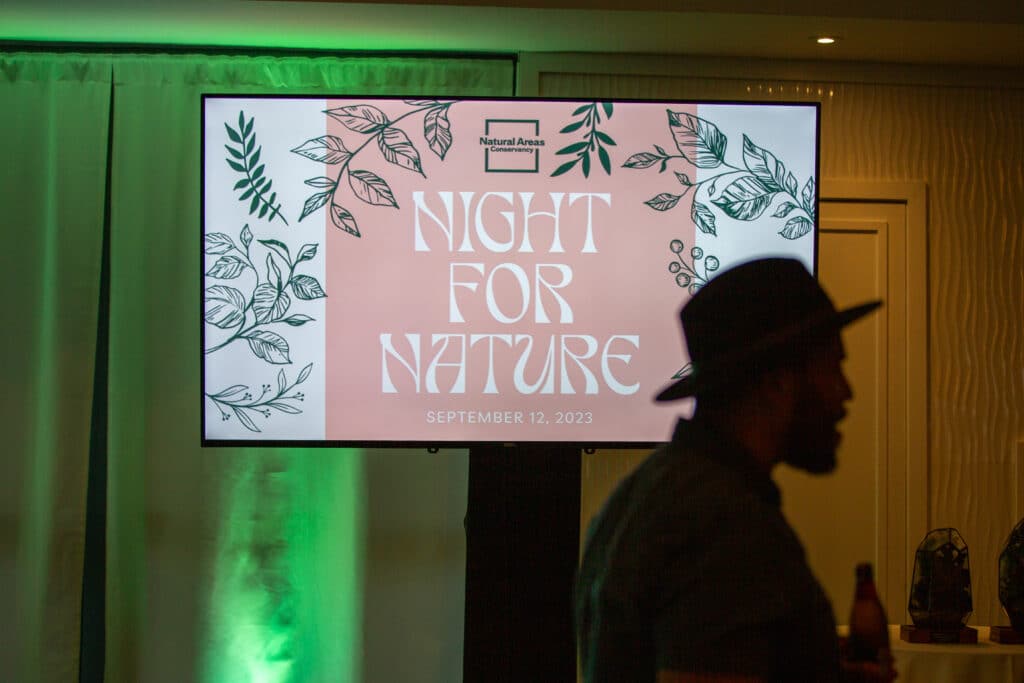 TV screen at 2023 Night for Nature with NAC staff member in the foreground